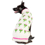Dog wearing a white sweater with green frog patterns on a white background
